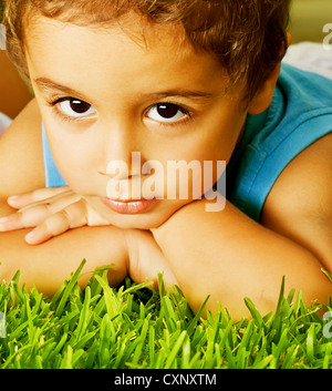 Photo de grave mignon petit garçon couché sur l'herbe verte fraîche, adorable bébé s'amusant en garderie, de l'homme composite Banque D'Images