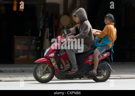 Un garçon regarde son père alors que sa mère leurs promenades en tenant une boîte de marchandises. Luang Prabang, Laos. Banque D'Images