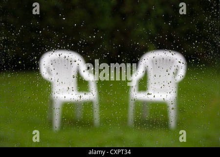 Hors foyer chaises de jardin vue à travers une fenêtre couverte de gouttes de pluie Banque D'Images