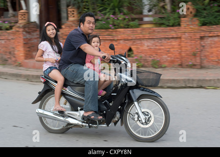 Un père et ses deux enfants passent sur une moto à Luang Prabang, Laos Banque D'Images