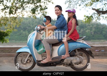 Une mère et ses deux enfants passent sur son scooter à Luang Prabang, Laos Banque D'Images