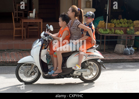 Une mère et ses deux enfants passent sur son scooter à Luang Prabang, Laos Banque D'Images