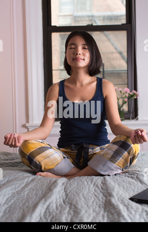 Jeune femme assise sur le lit et méditant Banque D'Images