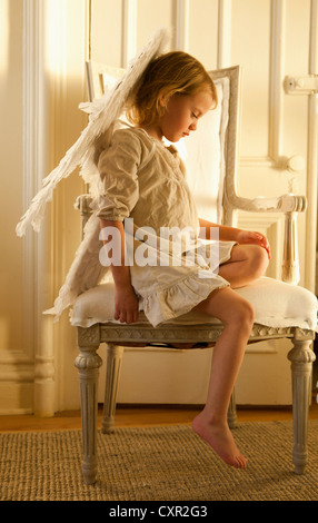 Petite fille sur une chaise habillée en ange Banque D'Images