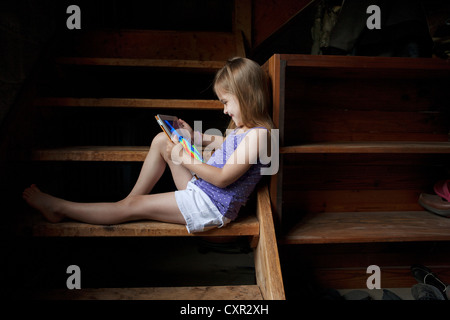 Petite fille assise sur les marches du sous-sol, looking at digital tablet Banque D'Images