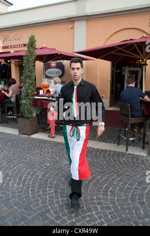 Un serveur portant un plateau de boissons portant son tablier aux couleurs du drapeau italien dans la ville de Bardolino, une station balnéaire/port de pêche dans la victoire rouge Banque D'Images