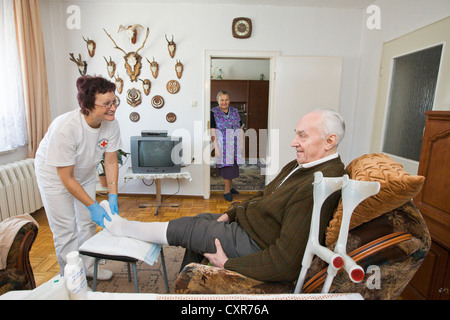 Les soins ambulatoires de l'infirmière de la Croix-Rouge allemande, Anke Lehmann assistant à un couple de personnes âgées, de changer le pansement sur son mari. Banque D'Images