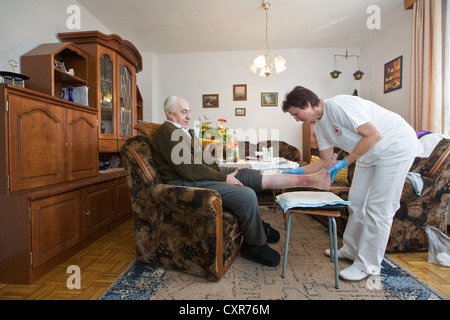 Les soins ambulatoires de l'infirmière de la Croix-Rouge allemande, Anke Lehmann assistant à un couple de personnes âgées, de changer le pansement sur son mari. Banque D'Images