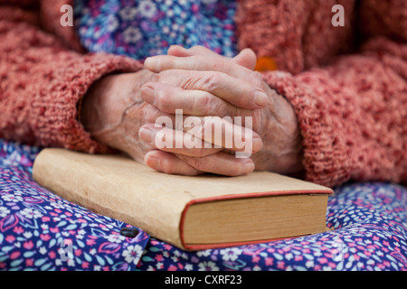 Mains jointes d'une vieille femme couchée sur ses genoux sur un livre Banque D'Images