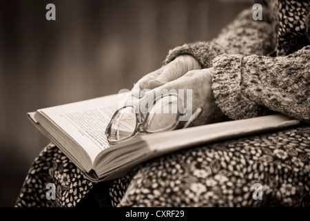 Mains d'une vieille femme tenant vieux verres sur un livre, le traitement sépia Banque D'Images