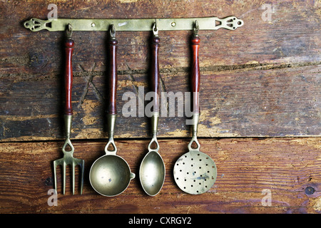 Ustensiles de cuisine anciens en laiton suspendue à un bar en face d'un mur en bois rustique Banque D'Images