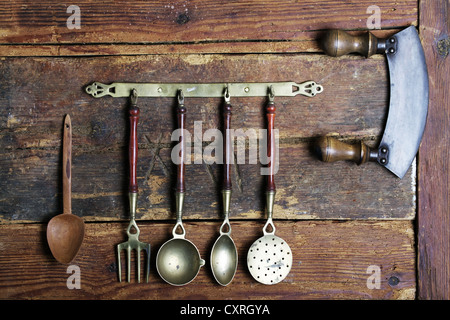 Ustensiles de cuisine anciens en laiton suspendue à un bar en face d'un mur en bois rustique Banque D'Images