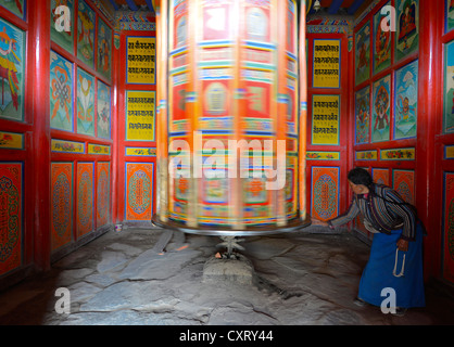 Le bouddhisme tibétain, un moulin à prière en bois peints avec des symboles bouddhistes est tourné par une vieille femme tibétaine Banque D'Images