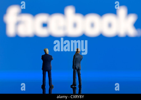 Deux hommes d'affaires, des figures miniatures debout devant un logo Facebook brouillée, image symbolique Banque D'Images