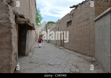 Femme musulmane bien que marche une ruelle dans la vieille ville de l'ancien quartier ouïghour, l'architecture de brique d'adobe, Route de la soie, Kashgar Banque D'Images