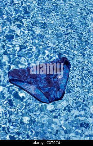 Maillot de bain bleu flottant à la surface d'une piscine extérieure, d'image symbolique pour les vacances ou les jours fériés Banque D'Images