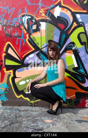 Jeune femme portant un haut turquoise, guêtres noires et de hauts talons en face de mur de graffiti Banque D'Images