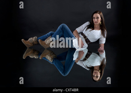 Jeune femme portant un haut blanc et un jean, allongé sur une image en miroir, miroir Banque D'Images