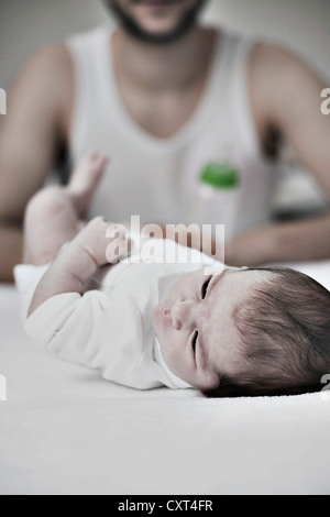 Père tenant une bouteille de lait dans sa main devant son nouveau-né allongé sur une table à langer Banque D'Images
