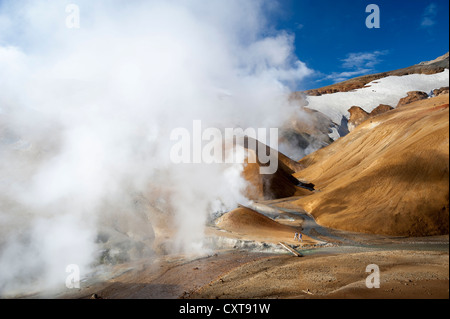 Les randonneurs sur un sentier, pont au-dessus d'un ruisseau à la vapeur, des sources chaudes et les sommets enneigés des montagnes de Rhyolite Banque D'Images