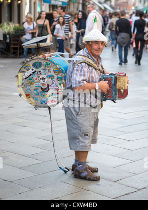 Un one man band jouant un accordéon concertina ou petite,cymbales, grosse caisse et d'un entonnoir avec des cloches sur sa tête. Banque D'Images