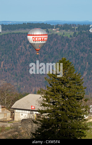 Hot Air Balloon volant à basse altitude au-dessus d'une ferme dans les montagnes du Jura, Suisse Banque D'Images