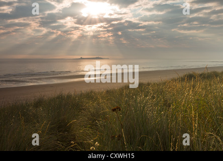 Plage de Bamburgh en regardant vers l'îles Farne, la lumière du soleil filtrant à travers les nuages, Northumberland, tôt le matin, l'été, Banque D'Images