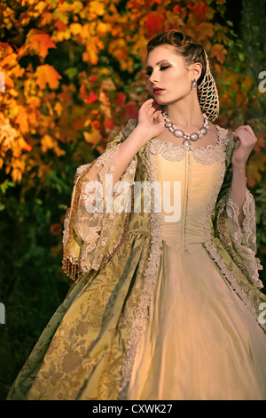 Une jeune femme brune habillée d'une robe vintage fantaisie debout devant des arbres d'automne Banque D'Images