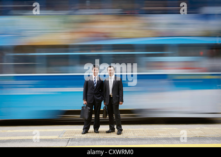 Businessmen standing by blurred bus Banque D'Images