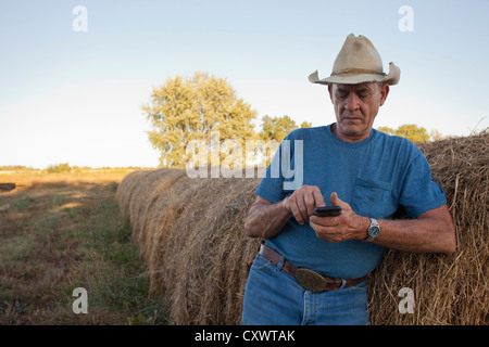 Farmer using cell phone par hay bales Banque D'Images