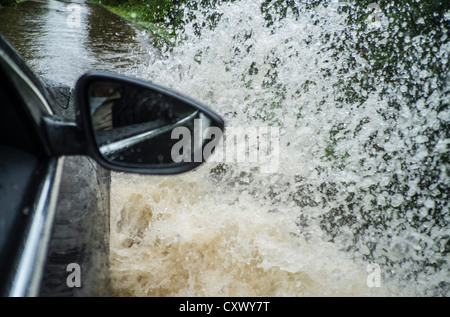 Les fortes précipitations entraînant des inondations localisées qu'une voiture fait son chemin à travers une route inondée au Royaume-Uni Banque D'Images