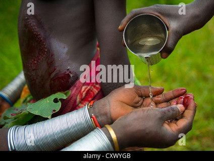 Suri Femme laver ses mains du sang après une cérémonie de la scarification, vallée de l'Omo, Ethiopie, Ethiopiatulgit Banque D'Images