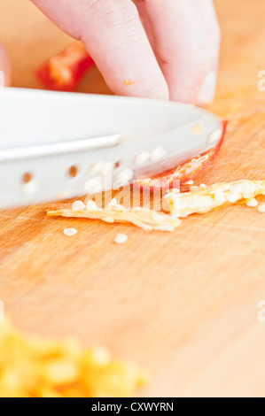 Gros plan du piment rouge haché en cours par un chef cuisinier sur une planche à découper en bois Banque D'Images