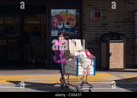 Une jeune femme hispanique de l'embonpoint pousse un panier chargé avec du lait et les sacs d'un supermarché à New York, USA. Banque D'Images