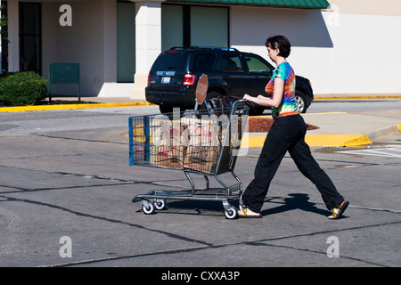 Une jeune femme de race blanche pousse un panier avec de la nourriture licenciés dans une aire de stationnement. Oklahoma City, Oklahoma, USA. Banque D'Images