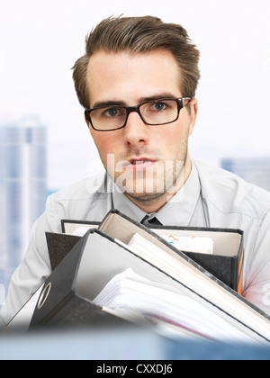 Young businessman wearing glasses transportant des fichiers de documents, visage sérieux, surmené Banque D'Images