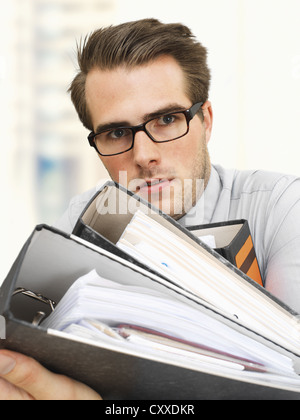 Young businessman wearing glasses transportant des fichiers de documents, visage sérieux, surmené Banque D'Images