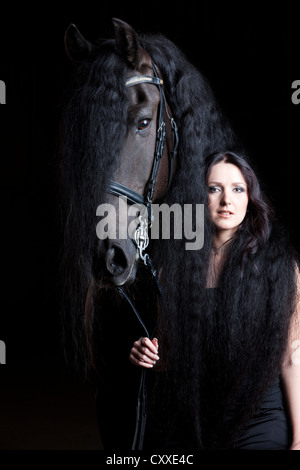 Frison frisons ou race avec jeune femme enveloppée dans sa longue crinière, cheval hongre, cheval noir Banque D'Images