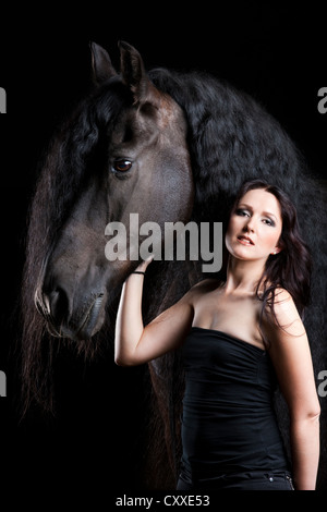 Frison frisons ou race avec jeune femme, cheval hongre, cheval noir Banque D'Images