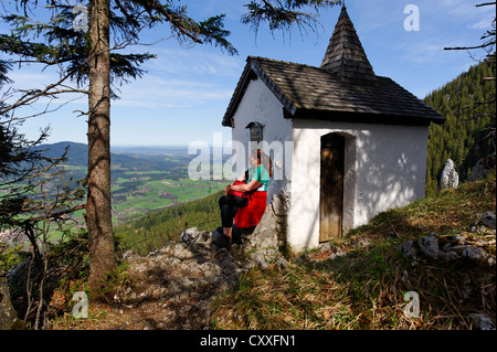 Les randonneurs assis en face d'une chapelle sur Kesselalm alp, Breitenstein Mountain, près de Fischbachau, Leitzachtal vallée, Haute-Bavière Banque D'Images