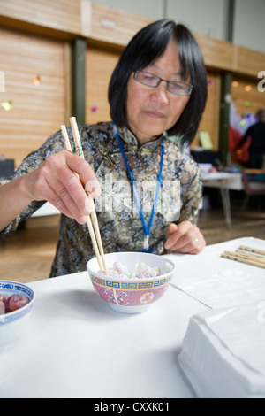 Femme chinoise portant des lunettes mangeant de bol de riz avec paire de baguettes Banque D'Images