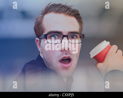 Young businessman wearing glasses, tenant une tasse de café, visage surpris Banque D'Images