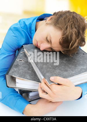 Jeune homme dormir sur une pile de dossiers Banque D'Images