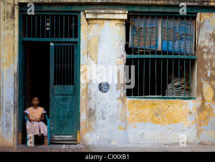 Petite fille qui s'ennuie assis sur une chaise en plastique bleu sur la porte d'une vieille maison coloniale à Chennai, Inde Banque D'Images