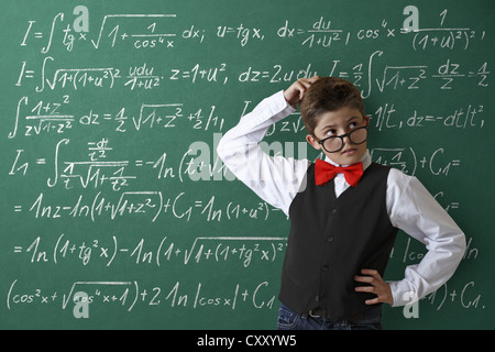 Impuissants à collégien portant des lunettes et une cravate d'arc en face d'un tableau avec les équations mathématiques Banque D'Images