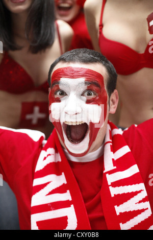 Jeune homme hurlant, fan de football avec un visage peint, drapeau national suisse Banque D'Images