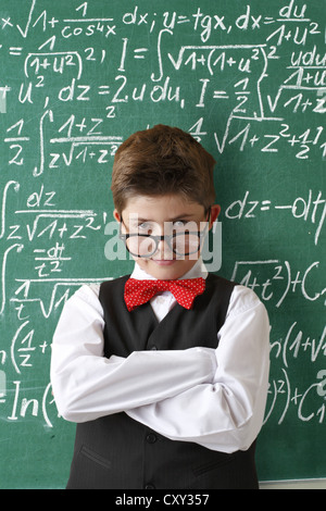 Écolier portant des lunettes et une cravate d'arc en face d'un tableau avec les équations mathématiques Banque D'Images