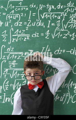 Impuissants à collégien portant des lunettes et une cravate d'arc en face d'un tableau avec les équations mathématiques Banque D'Images