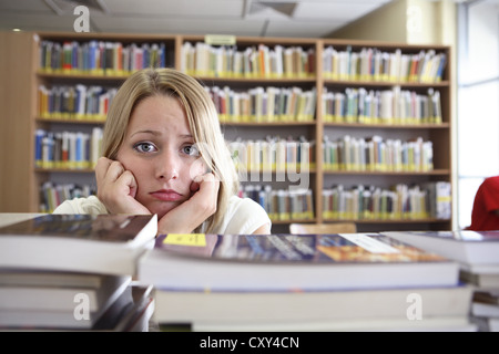 Étudiant frustré à plus de piles de livres, la bibliothèque de l'université Banque D'Images