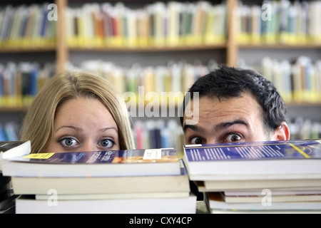 Les étudiants, paire, à la recherche de derrière des piles de livres, la bibliothèque de l'université Banque D'Images